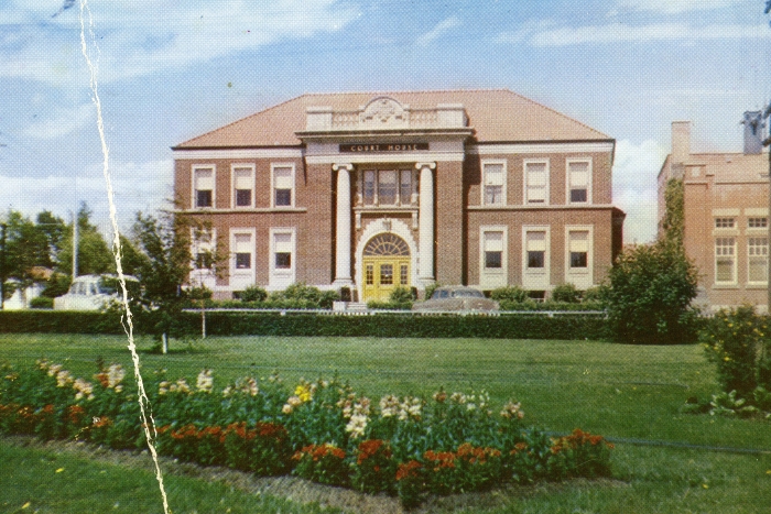 Colour photo of the Old Red Deer Court House, a two storey brick building with white columns in front, with green grass and