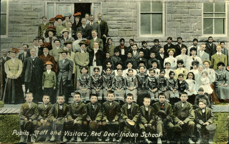 Colourized postcard photo showing the students, staff, and important visitors in front of the main building at the Red Deer Indian Industrial School, 1911.