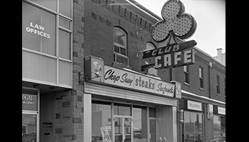 Black and white photo of a sign for the Club Cafe in Red deer, including a large club-shape from playing cards.