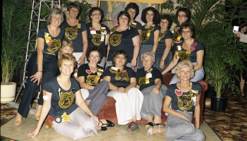 Colour photo of a group of women posing under a sign for the Red Deer Oil Wives in 1980.