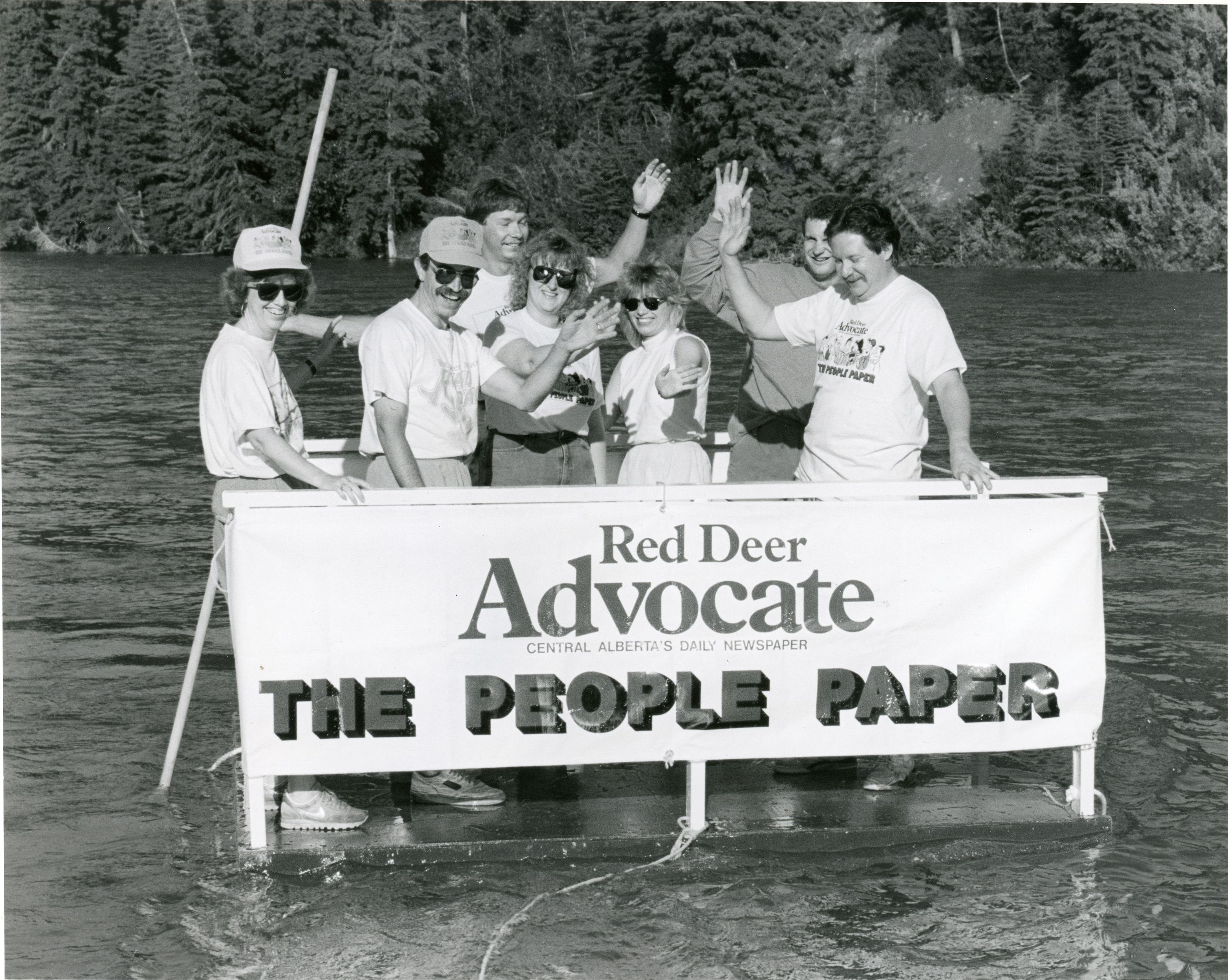 Black and white photo of a group of people standing behind a sign that says