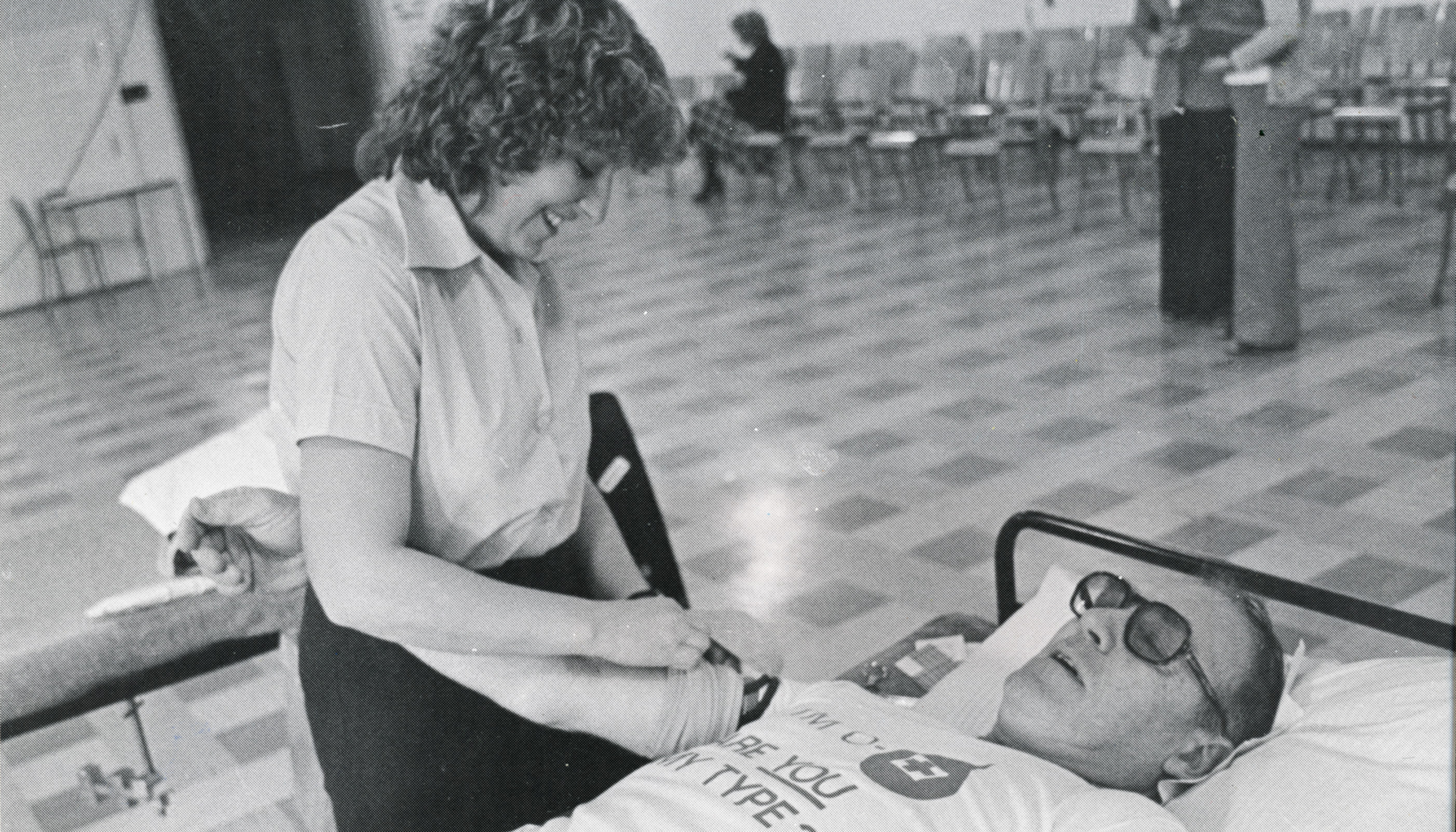 Black and white photo of a woman taking a blood donation from a man who is lying on a bed.