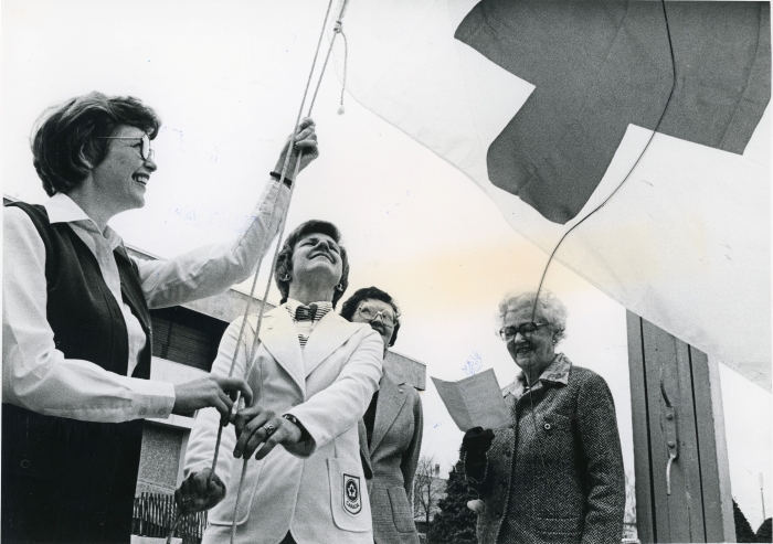 Black and white photo of four people raising a Red Cross flag at City Hall in Red Deer, Alberta in 1979.