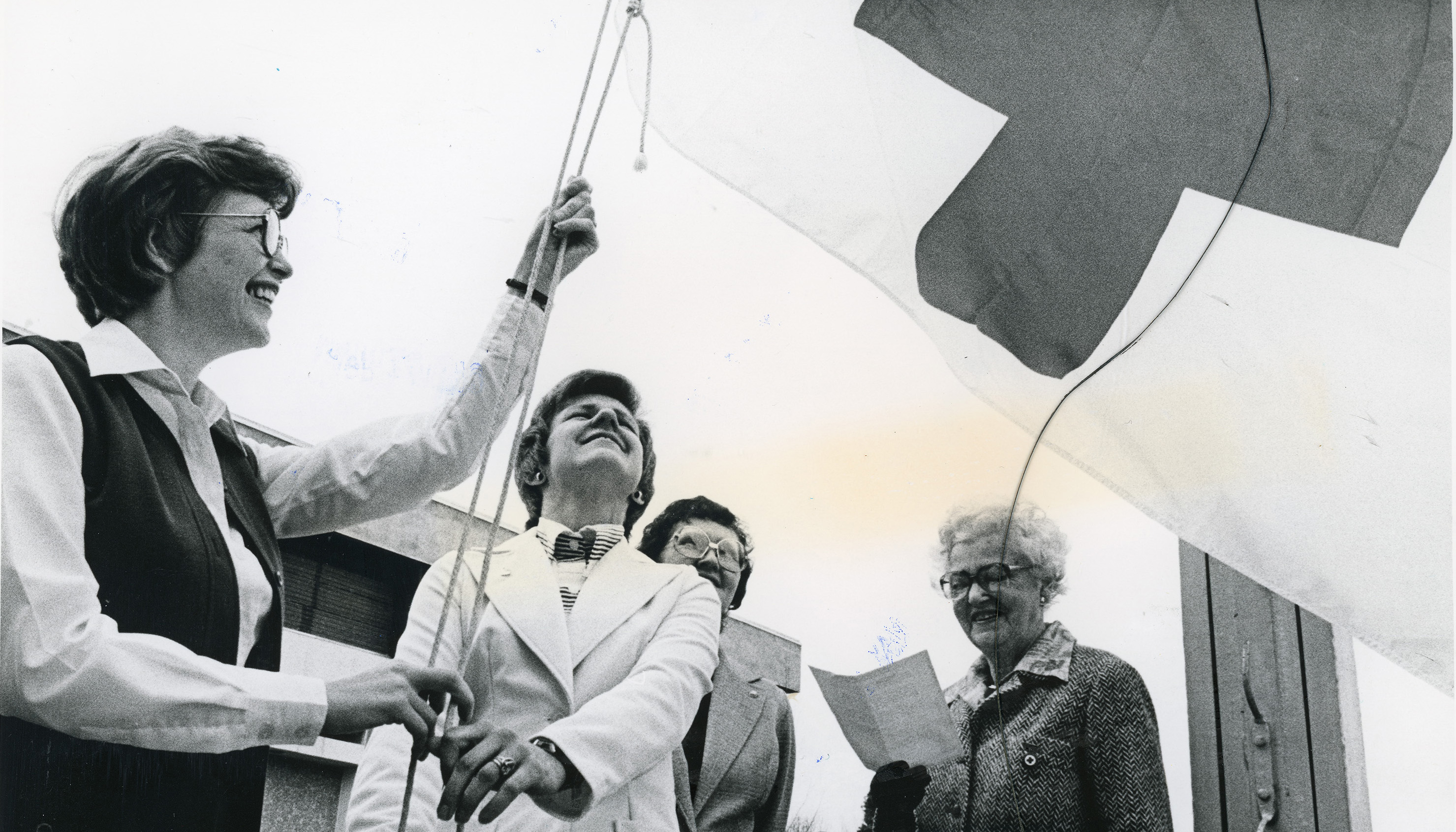 Black and white photo of four people raising a Red Cross flag at City Hall in Red Deer, Alberta in 1979.