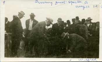 Black and white photo of Sir Wilfrid Laurier driving the first spike for the Alberta Central Railroad in Red Deer with blue writing on the photo