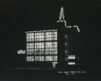 Black and white photo taken from 43 street of the front side of the Red Deer Brewing Co. building in Red Deer, Alberta. The building has decorative lights and a Christmas tree on the roof.