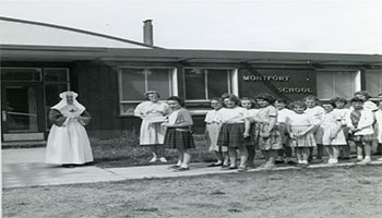 Black and white photo of Sister Ruth and school children in front of Monfort School during a fire drill