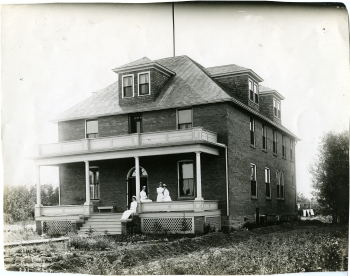 Black and white photo of the exterior of the Red Deer Memorial Hospital with four nurses on the veranda