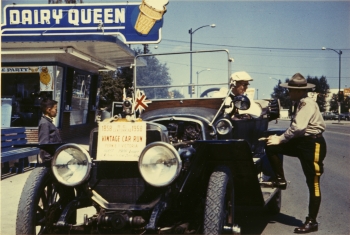 Coloured photo of Charlie Parker in his 1908 Lozier Touring Car with a RCMP officer who appears to be pretending to give him a ticket
