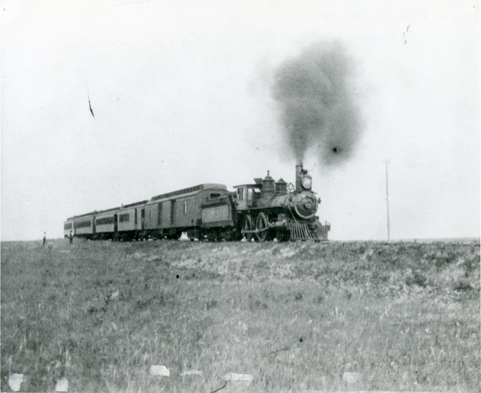 Black and white photo of a steam train with three cars behind it on the prairies, 1892