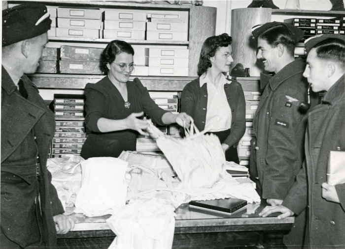 Black and white photo of a group of soldiers in winter coats shopping in a ladies wear store in Red Deer with two women assisting them.
