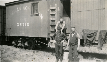 Black and white photo of three workers in front of a Canadian Northern Rail car No. 35710 in Alberta