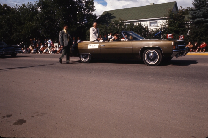 Colour photo of a man sitting in the back of an open-top green car during a parade, 1972