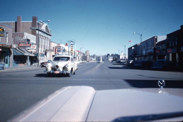 Colour photo of Ross Street in 1961 with two way traffic and various buildings shown with a blue sky.