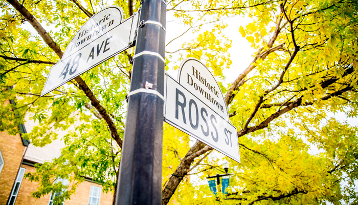 A street sign at the intersection of Ross Street and 48 Avenue taken in the fall, with colourful leaves in the background.