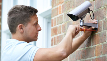 Photo of person installing surveillance camera on outside brick wall