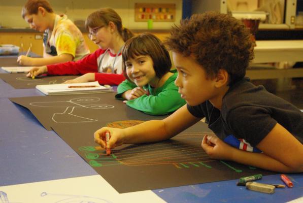 Photograh of four children around the age of eight drawing on black paper with colourful pastels in the Visual Art Studio at Culture Services.