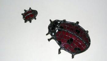 Glass mosiac tiles in the shape of two lady bugs, one big and one little on a wall.